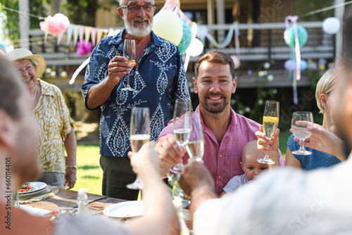 Big family clinking glasses at a garden party. Celebratory toast at the table.