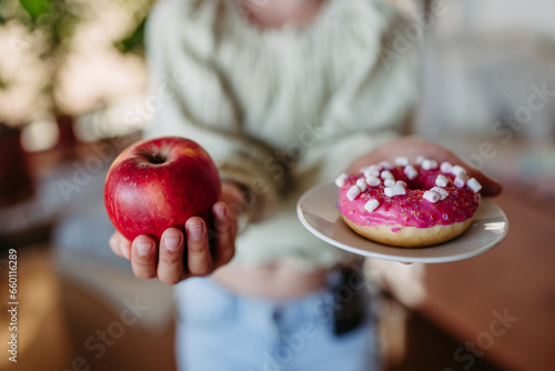 Fotografie Diabetic woman is choosing between fresh apple and a sweet doughnut