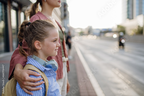 Fototapeta Mother and school girl with backpack holding hands while crossing busy road