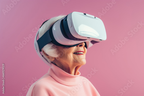 Cute elderly cheerful woman wearing modern VR goggles on pink pastel background.