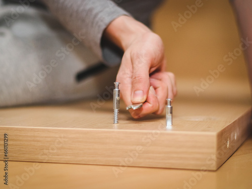 The hands of a caucasian young man with a wrench tighten a bolt on the wooden part of the bed