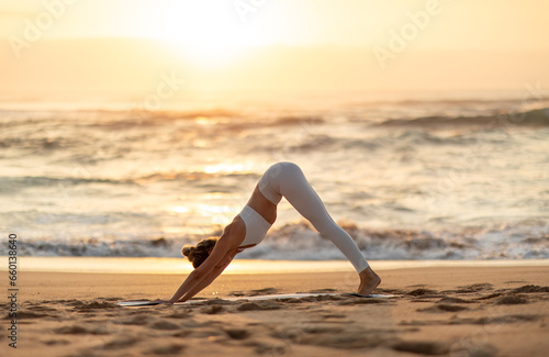 Young fit caucasian woman practicing yoga, doing exercise, asana enjoying workout on sea beach at sunset, side view