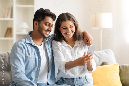 Young Indian couple using smartphone at cozy home interior
