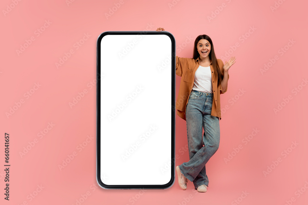 Great Offer. Excited Teen Girl Standing Near Blank Smartphone With White Screen Great Offer. Excited Teen Girl Standing Near Blank Smartphone With White Screen
