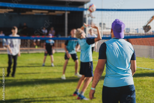 Volleyball game, junior teenage school team of kids play volleyball, players on the outdoor playground with net and green lawn grass court, sports children team during the game, summer sunny