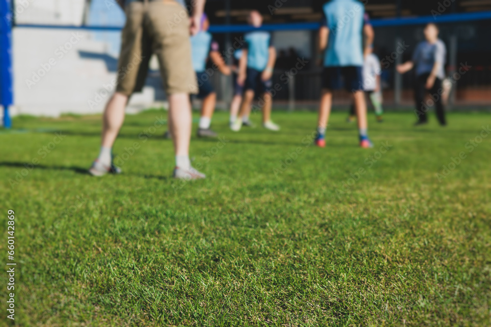 Fototapeta premium Volleyball game, junior teenage school team of kids play volleyball, players on the outdoor playground with net and green lawn grass court, sports children team during the game, summer sunny