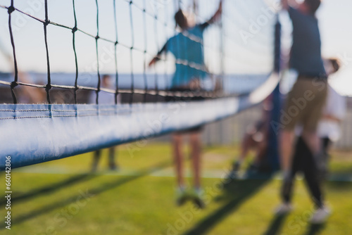 Fototapeta Naklejka Na Ścianę i Meble -  Volleyball game, junior teenage school team of kids play volleyball, players on the outdoor playground with net and green lawn grass court, sports children team during the game, summer sunny