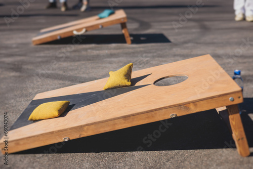 Cornhole game set, process of throwing bean bags, kids children tossing bean sacks, corn hole in the backyard, wooden boards for corn-hole tournament in the summer sunny day