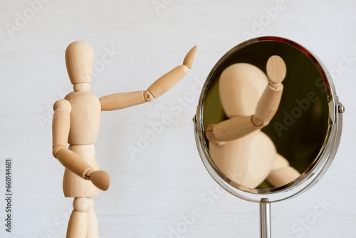 A light wooden mannequin looks in the mirror, looking for its image. The concept is self-knowledge, self-esteem.
