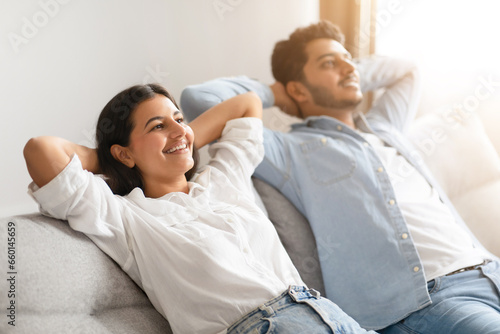 Photos Indian couple leisurely reclining on sofa, holding hands behind heads
