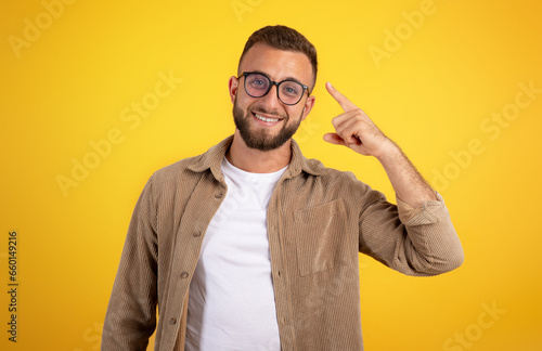 Happy smart confident millennial caucasian man with beard in casual and glasses point finger at head