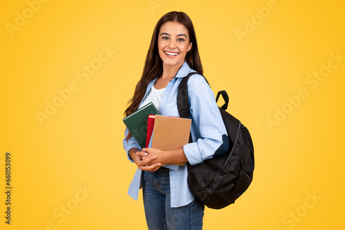 Woman student studying intently, surrounded by books, against a bright yellow backgroun