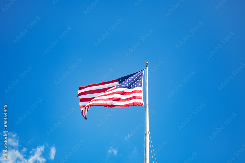 Fototapeta premium Mast with the flag of the United States of America against the blue sky.