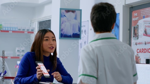 Asian customer at drugstore counter, showing druggist prescribed heart attack prevention medicine and inquiring about required dosage. Wellness expert helping client with needed medicinal product