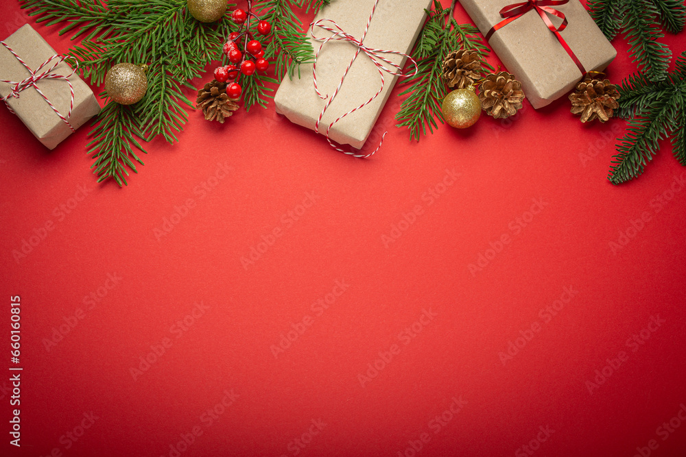 Fototapeta premium Christmas or New Year celebration red paper festive background with decoration fir tree, wrapped present boxes, cones, berries, sparkly red balls. Space for text..