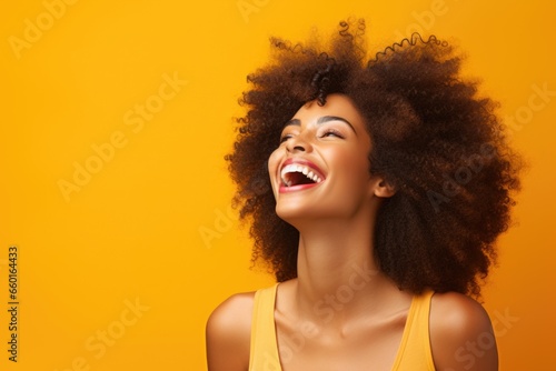 portrait of a smiling young woman laughing. young black woman with curly hair laughing on orange background