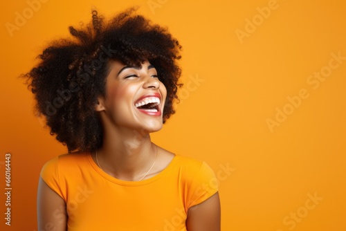 portrait of a smiling young woman laughing. young black woman with curly hair laughing on orange background photo