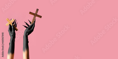 Black hands of witch with wooden crosses on pink background with space for text. Halloween celebration