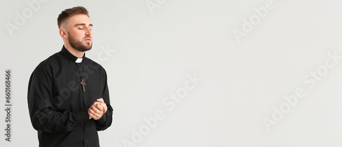 Young priest praying to God on light background with space for text