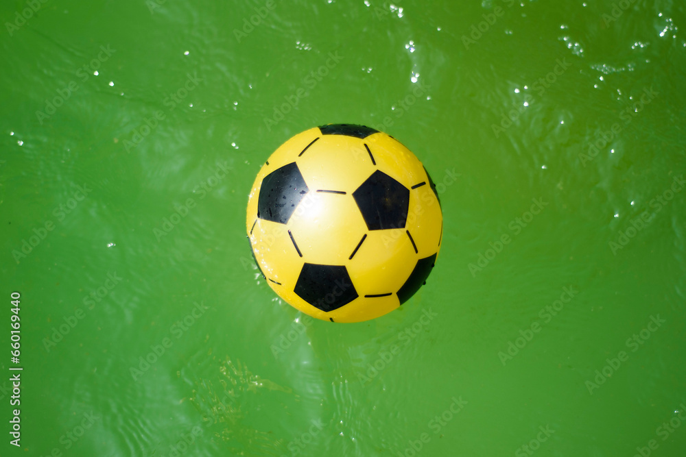 Fototapeta premium composition of a yellow plastic soccer ball on green water.