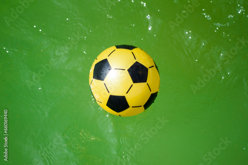 composition of a yellow plastic soccer ball on green water.