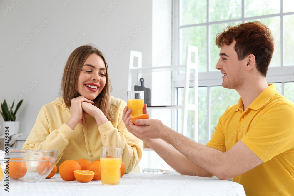 Young man giving glass of orange juice to his girlfriend in kitchen Young man giving glass of orange juice to his girlfriend in kitchen