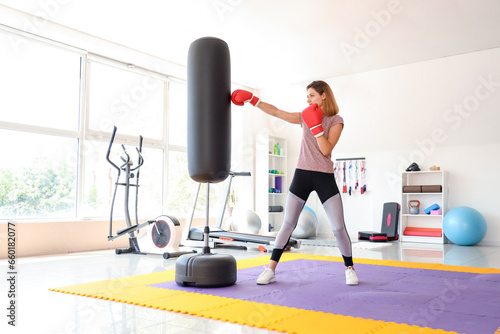 Young woman training with punching bag in gym. Concept of self defense
