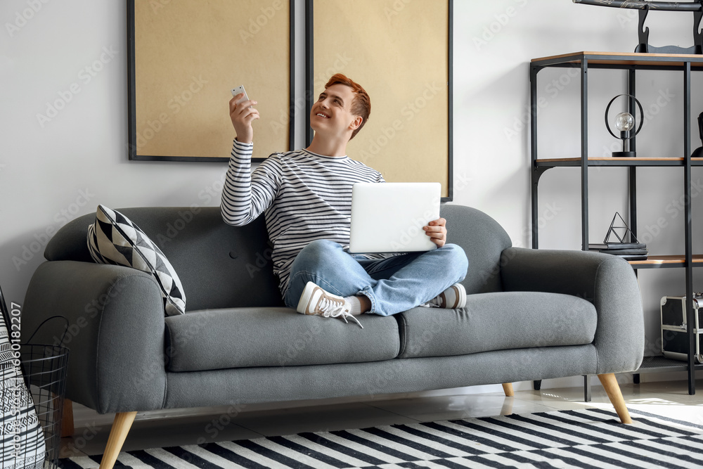 Young man with laptop switching on air conditioner at home Young man with laptop switching on air conditioner at home