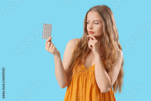 Thoughtful young woman with contraceptive pills on blue background