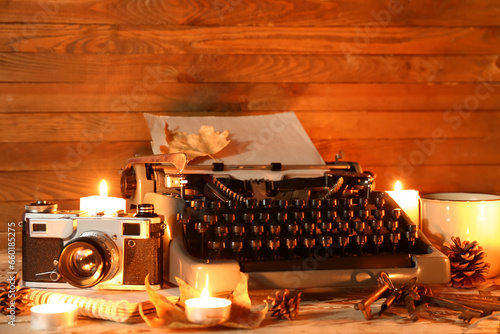 Vintage typewriter, photo camera, keys, pine cones, burning candles and autumn leaves on wooden background