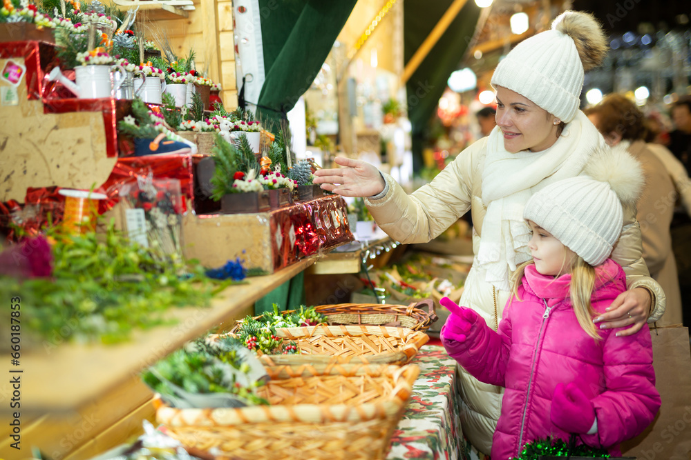 Young girl and her mother are buying Christmas ornamentals in the market outdoor. High quality photo