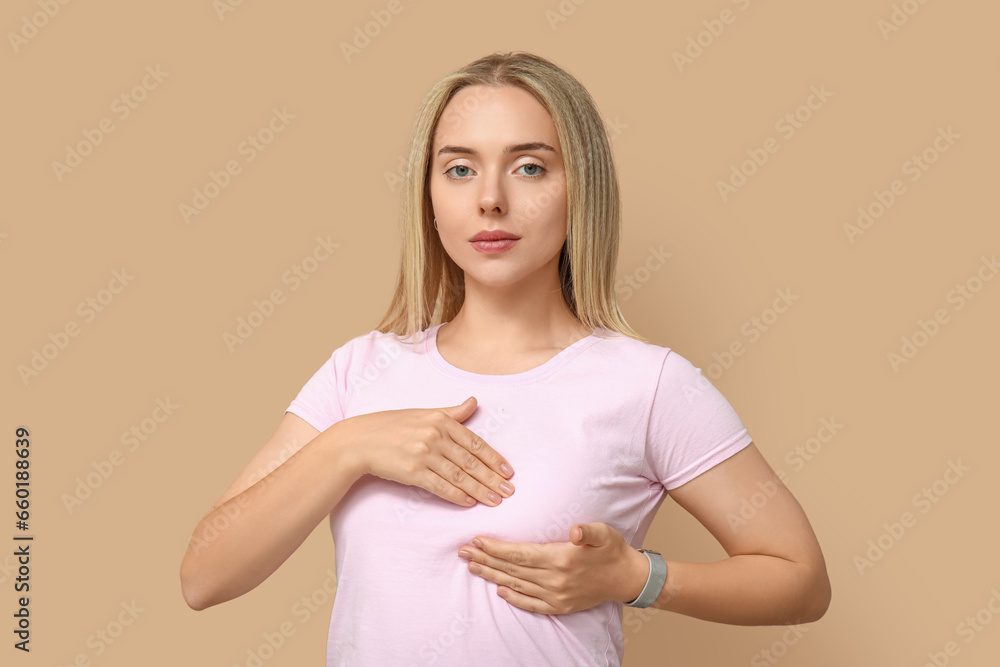 Obraz premium Young woman checking her breast on beige background. Cancer awareness concept
