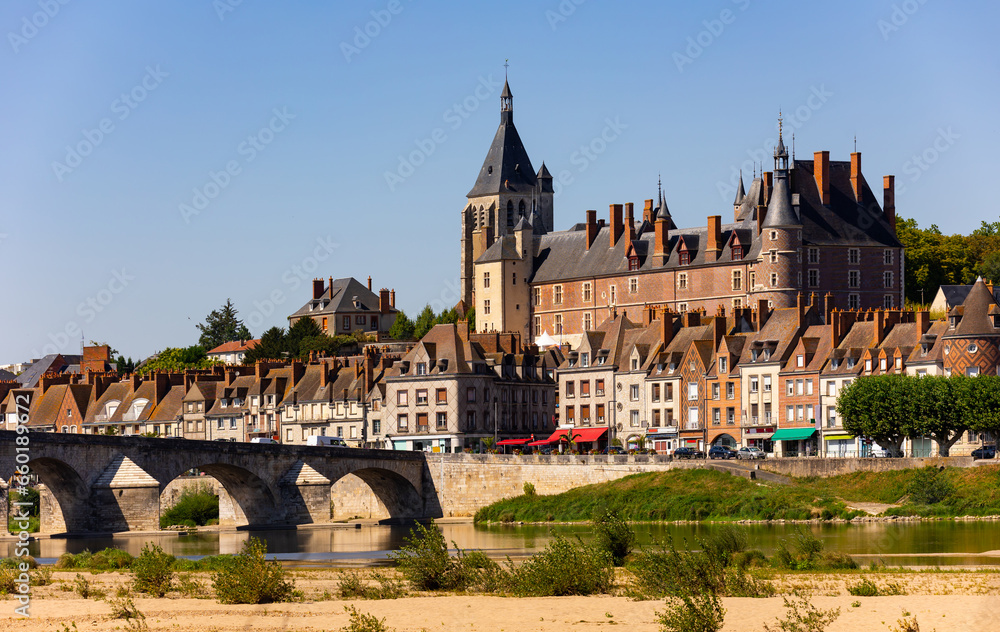 View of Gien cityscape on bank of Loire with row of townhouses along embankment, medieval renaissance castle and arched bridge across river on summer day, Loiret, France