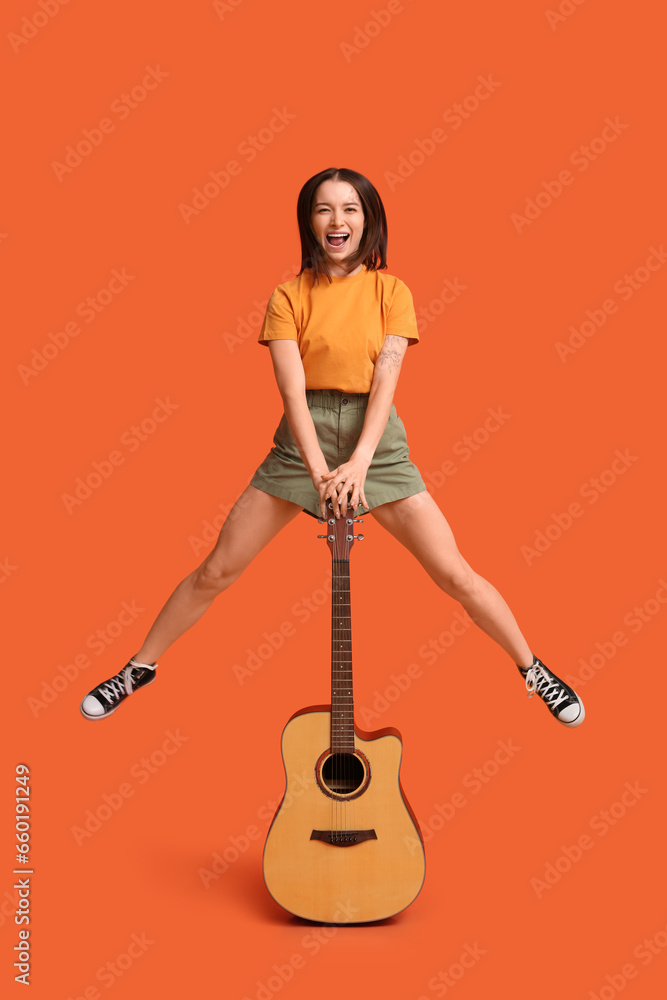 Obraz premium Pretty young woman with acoustic guitar on orange background