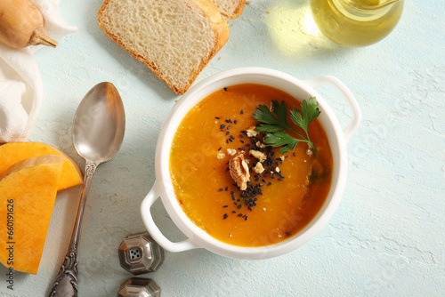 Pot of delicious pumpkin cream soup with walnut and parsley on light blue background