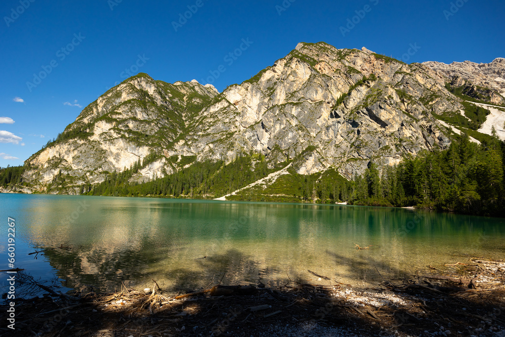 Breathtaking beauty of Pragser Wildsee, calm alpine lake Braies with emerald waters nestled amidst Dolomite mountains with towering rocky peaks on sunny summer day, Italy