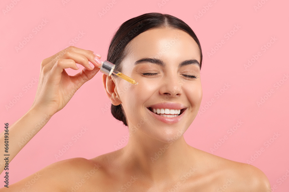 Beautiful young woman applying serum onto her face on pink background Beautiful young woman applying serum onto her face on pink background