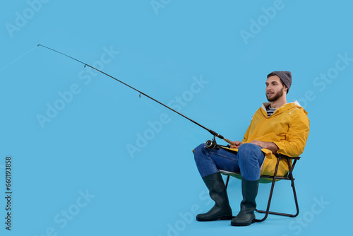 Fisherman with rod on fishing chair against light blue background