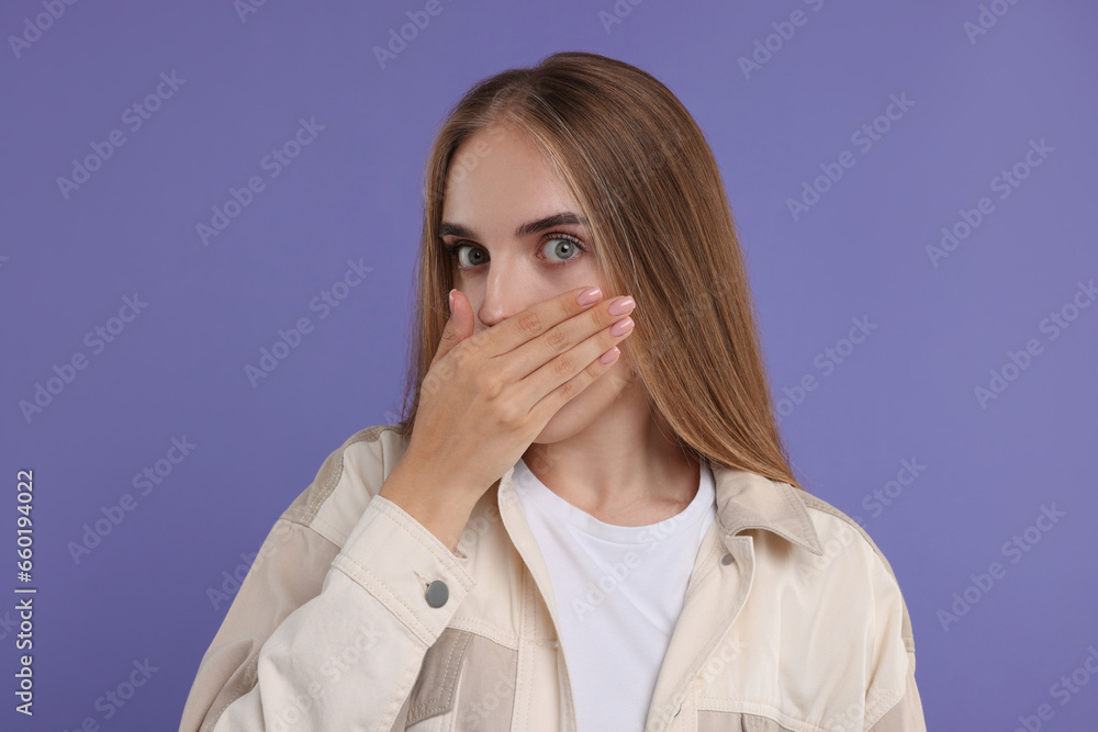 Embarrassed woman covering mouth with hand on violet background Embarrassed woman covering mouth with hand on violet background