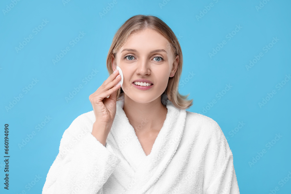 Young woman cleaning face with cotton pad on light blue background Young woman cleaning face with cotton pad on light blue background