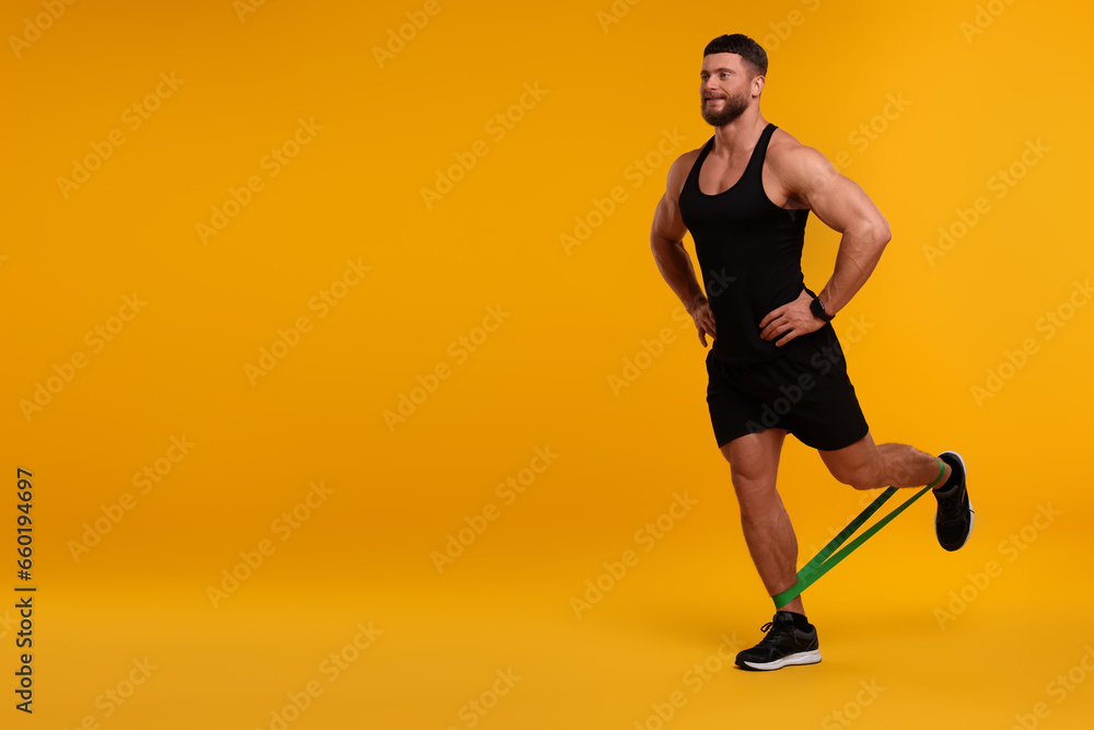 Young man exercising with elastic resistance band on orange background. Space for text