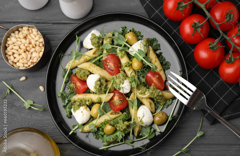 Delicious pesto pasta salad, ingredients and fork on gray wooden table, flat lay