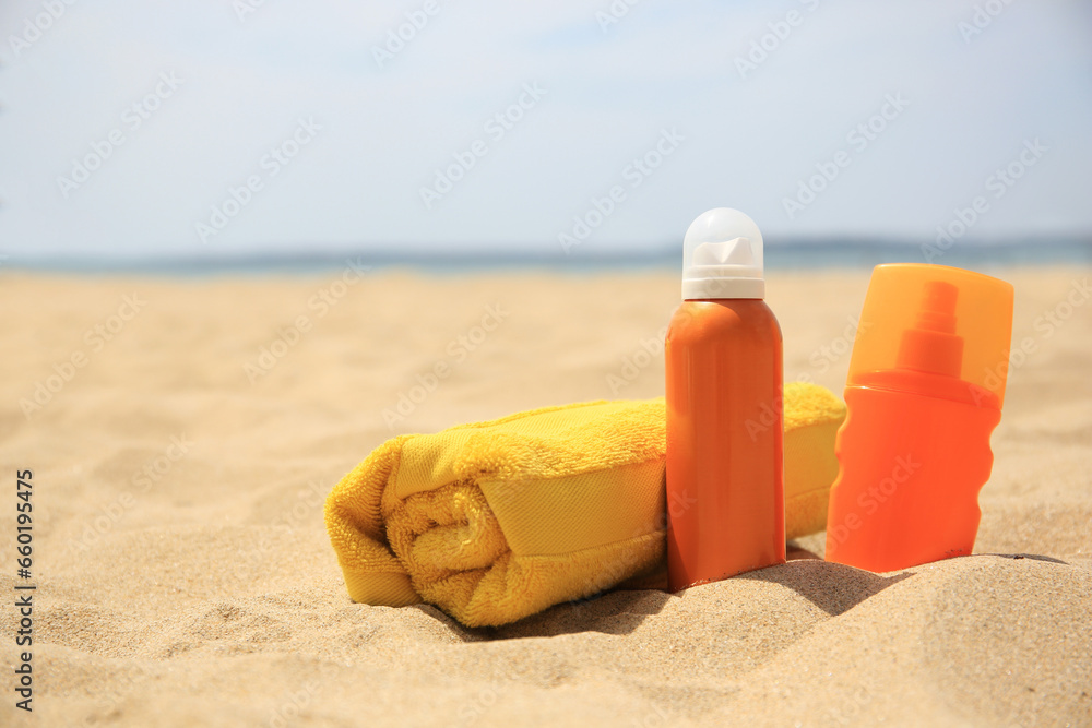 Sunscreens and rolled towel on sandy beach, space for text. Sun protection care Sunscreens and rolled towel on sandy beach, space for text. Sun protection care