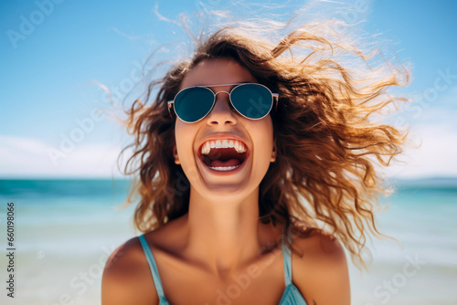 portrait of an attractive excited young woman in shades loving life smiling and having fun on the beach with the surf in the background having fun relaxing no cares or worries