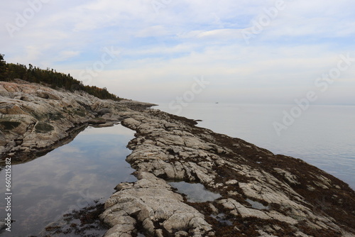 Beach and rocks in autumn. Riverside with stones. Reflect of water and river. Horizon and peaceful landscape.  A beautiful coastline in Charlevoix in Quebec. Environement and ecology. photo