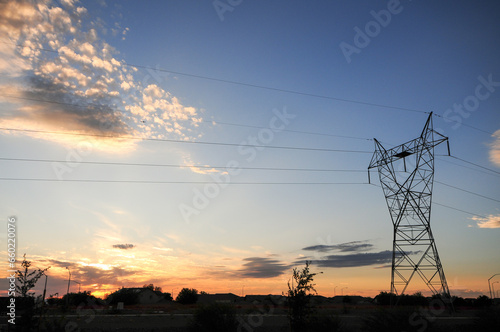 The silhouette of a pylon and power wires with the bright orange-yellow glow of the sunset as a backdrop