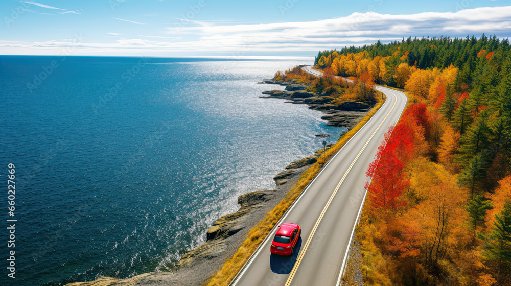 Aerial view of fall road and blue water lake sea ocean. Red car with a roof rack on a country road in Finland.
