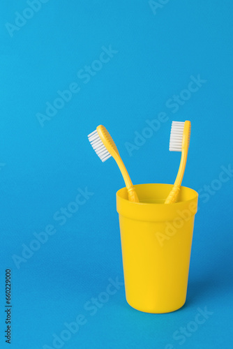 Two yellow toothbrushes in a yellow plastic cup on a blue background.
