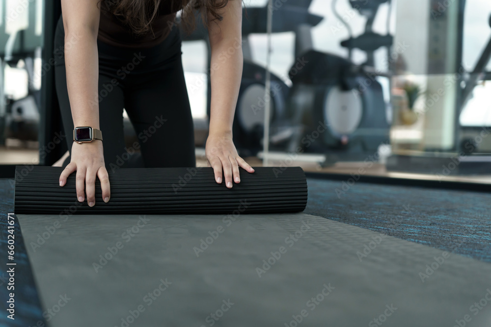 Fitness woman folding exercise mat before working out in yoga studio. rolling Yoga mat  after training healthy lifestyle