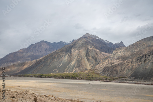 Scenic view of Himalayas and Ladakh ranges. Beautiful barren hills in Ladakh with dramatic clouds in the background.  Road side view, Shyok river , rocks and greenery in base of the mountains. photo